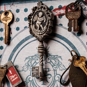 May include: An assortment of antique keys, including a large ornate key with an angel design, and keys labeled "LOUNGE & BAR" and "PANTRY." The background features a patterned design with a touch of red.