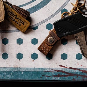 May include: Close-up of vintage keys and keychains. One key has "1054 WB" on it. Another keychain reads "Cedarbrook Apartments". The keys and keychains are on a patterned surface with teal and white geometric shapes.