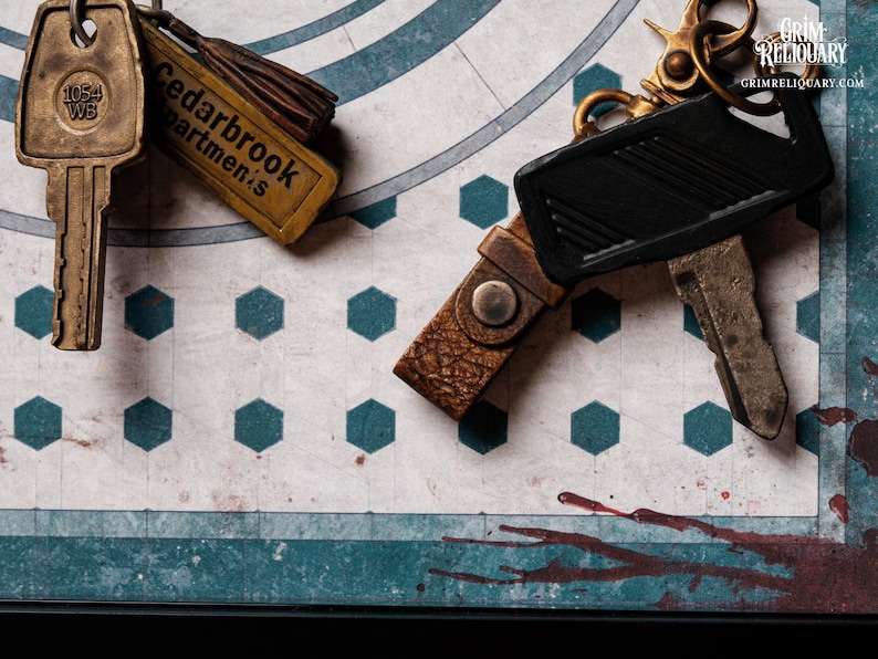 May include: Close-up of vintage keys and keychains. One key has "1054 WB" on it. Another keychain reads "Cedarbrook Apartments". The keys and keychains are on a patterned surface with teal and white geometric shapes.