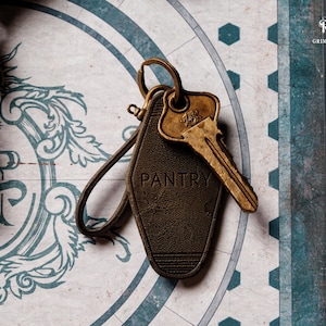 May include: A vintage-style key and key tag with the word "PANTRY" embossed on it. The key is gold-colored, and the tag is dark brown with a leather-like texture. The background features a decorative design with blue and white elements.