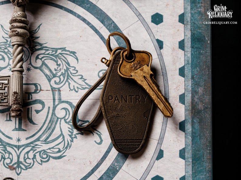 May include: A vintage-style key and key tag with the word "PANTRY" embossed on it. The key is gold-colored, and the tag is dark brown with a leather-like texture. The background features a decorative design with blue and white elements.