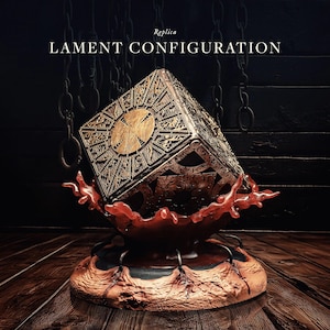 Może przedstawiać: Replika skrzynki z zagadkami Lament Configuration, kostki ze skomplikowanymi geometrycznymi wzorami i centralnym okrągłym wzorem. Kostka spoczywa na rzeźbionej podstawie z czerwonym, organicznie wyglądającym elementem. Widoczny jest tekst "LAMENT CONFIGURATION".