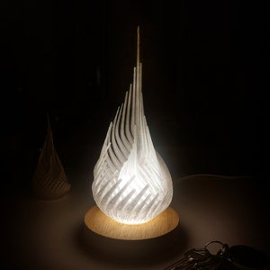 May include: A white, 3D printed lamp shaped like a flame with a wooden base. The lamp is lit and casting a warm glow.