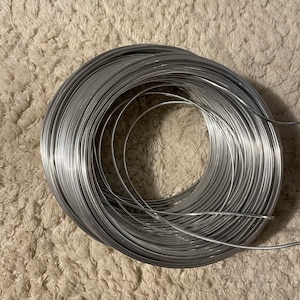 Könnte beinhalten: Eine Spule aus silberfarbenem Draht, fest zusammengerollt. Der Draht ist glatt und glänzend und wahrscheinlich aus Aluminium oder Stahl.