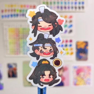 May include: Three cartoon character stickers with black hair, blue headbands, and white faces. The stickers are on a blue pen.