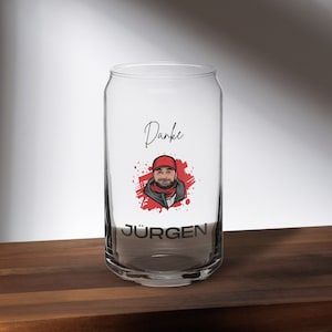 May include: A clear glass can with a red and black design. The design features a cartoon portrait of a person with a red hat and a black beard. The text "Danke" and "JÜRGEN" are printed on the can.