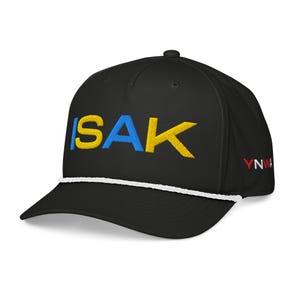 Op de afbeelding: Zwarte baseball cap met het woord "ISAK" geborduurd in blauw en geel. De cap heeft een wit touwdetail en de letters "YNWA" in rood aan de zijkant.