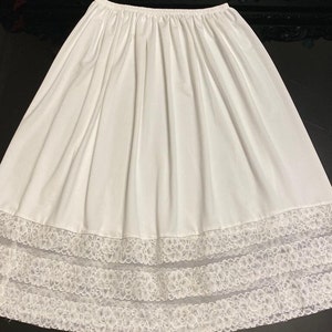 May include: A white cotton slip skirt with a lace trim. The skirt has a gathered waistband and a full, flowing silhouette.