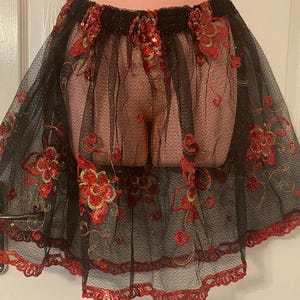 May include: Black tulle skirt with red and gold floral embroidery. The skirt has a scalloped hem and a black elastic waistband.