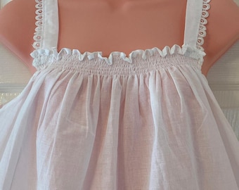 Puede incluir: Camisón blanco de algodón con ribete de encaje en las tiras. La parte superior del camisón tiene una banda elástica fruncida.