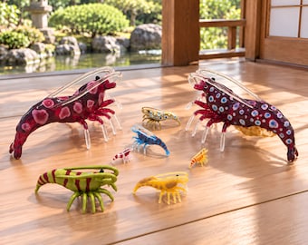 Puede incluir: Una colección de siete figuras de camarones de vidrio en varios tamaños y colores. Dos camarones grandes tienen cuerpos de color púrpura oscuro con manchas rosas o azules. Los más pequeños son de color verde a rayas, azul, amarillo o rojo y blanco.