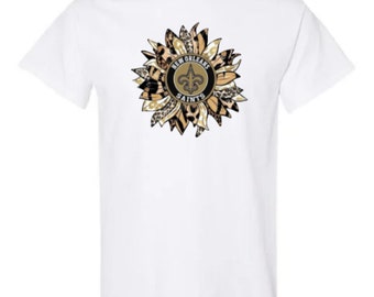May include: White t-shirt with a sunflower design featuring the New Orleans Saints logo. The sunflower is made up of leopard print and gold fabric.