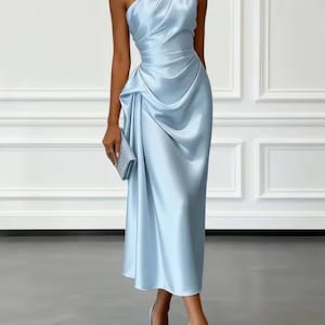 Pode incluir: Um vestido midi de cetim azul claro com decote de um ombro só, detalhes de tecido franzido na cintura e saia drapeada. A peça é combinada com sapatos de salto azul claro de bico fino e uma pequena bolsa clutch retangular prateada.