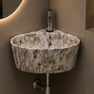 May include: A corner-mounted bathroom sink featuring a white marble pattern with gold-toned veining. The basin is equipped with a single chrome tap and a matching chrome drain pipe extending from the bottom centre of the sink unit.