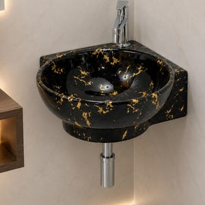 May include: A wall-mounted corner sink featuring a glossy black finish with irregular gold-colored flecks throughout. The basin is circular with a chrome faucet installed at the back corner and a matching chrome drain pipe extending downward.