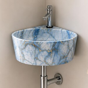 May include: A corner-mounted bathroom sink featuring a blue and white marble pattern with gold veining. The basin is equipped with a polished chrome faucet and a matching chrome drain pipe extending from the bottom towards the wall.