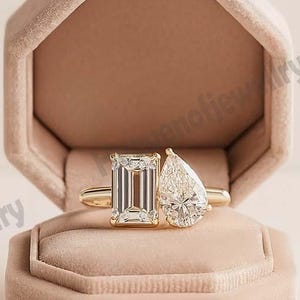 Peut inclure: Une bague en or avec deux pierres précieuses claires : une taille émeraude et une forme de poire. La bague est présentée dans un écrin de forme octogonale en velours pêche ouvert.