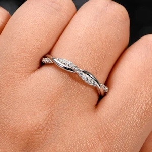 May include: A delicate silver band ring with a twisted design and small clear stones.
