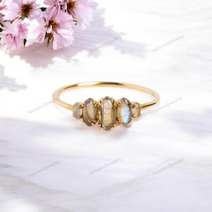 May include: A gold ring with four oval-shaped labradorite gemstones. The ring is set on a white background.