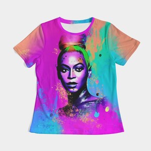 May include: A vibrant, short-sleeved t-shirt featuring a portrait of a woman with a high bun. The artwork is rendered in a watercolor style with a vivid color palette of pink, purple, blue, and orange. The shirt has a round neckline.