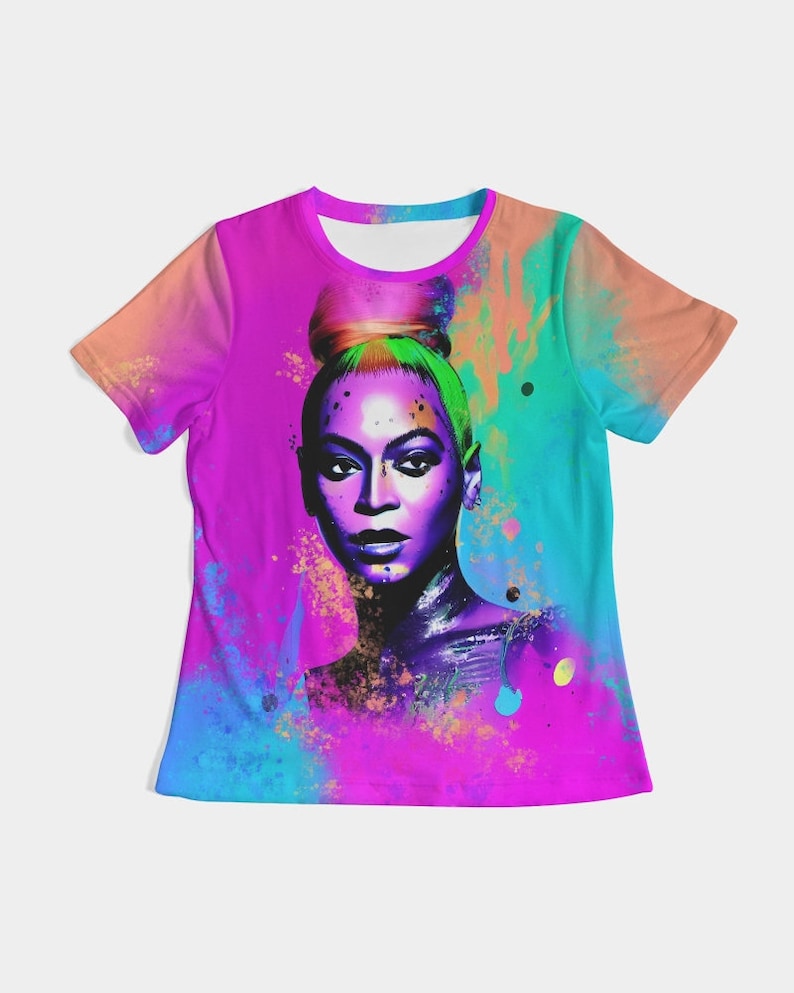 May include: A vibrant, short-sleeved t-shirt featuring a portrait of a woman with a high bun. The artwork is rendered in a watercolor style with a vivid color palette of pink, purple, blue, and orange. The shirt has a round neckline.