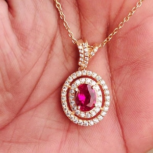 May include: A gold necklace with a pendant featuring a large oval ruby surrounded by a double halo of smaller diamonds.