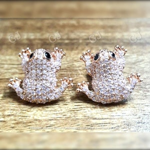 May include: A pair of rose gold frog stud earrings with black eyes and clear cubic zirconia stones.