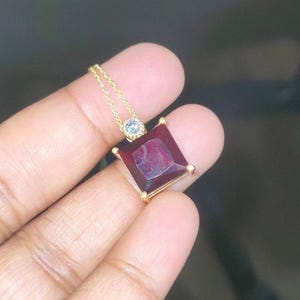May include: A gold pendant necklace with a large, square, red gemstone and a smaller, round, clear gemstone.