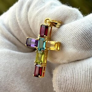 Pode incluir: Um pingente de cruz de ouro com pedras preciosas coloridas. A cruz é adornada com pedras preciosas vermelhas, roxas, azuis, verdes e amarelas.