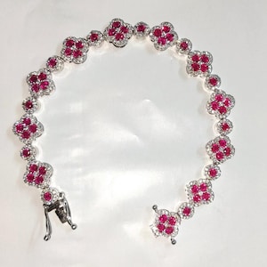May include: A silver bracelet with a delicate chain and red ruby stones set in a clover shape.