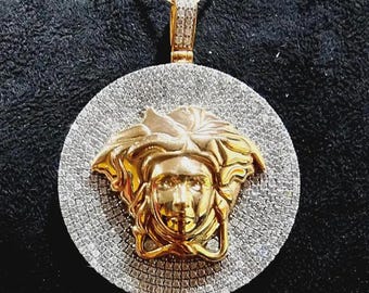 May include: A gold and silver pendant necklace featuring a Medusa head design. The pendant has a gold Medusa head in the center, surrounded by a circle of small, sparkling stones. The necklace chain is silver.