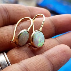 Puede incluir: Un par de pendientes de oro con piedras de ópalo blanco de forma ovalada. Los pendientes tienen un diseño simple y elegante.