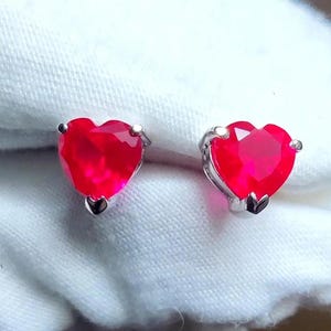 Puede incluir: Un par de pendientes en forma de corazón con piedras preciosas rojas engastadas en plata.