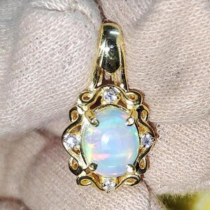 May include: A gold pendant featuring an oval opal gemstone. The opal has a milky white base with iridescent flashes of color. The pendant is accented with small, clear gemstones and ornate gold detailing.