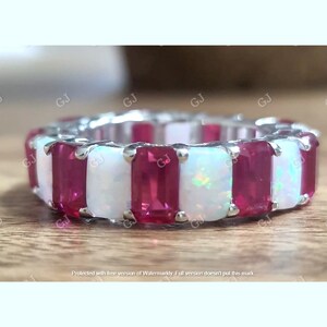 May include: A silver band ring with alternating red ruby and white opal stones. The stones are rectangular and set in a prong setting.