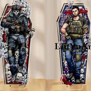 Pode incluir: Duas peças de arte em acrílico em forma de caixão. Uma apresenta um soldado com uma máscara de caveira segurando um rifle, rodeado por caveiras e flores. A outra retrata um soldado com um colete tático, rosas e caveiras. O texto "UYUART" é visível.