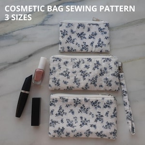 May include: Cosmetic bag sewing pattern in three sizes. The bags are white with a blue floral pattern. The image also shows a tube of mascara, a bottle of nail varnish, and a lipstick. The bags have a zip closure.