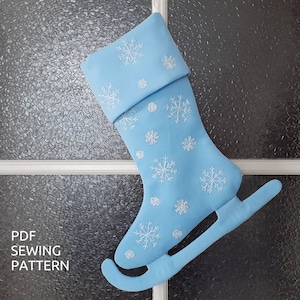 May include: A light blue Christmas stocking shaped like an ice skate with white snowflake embroidery. The stocking has a cuff and a blade.