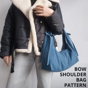 Può includere: Una borsa a tracolla in denim blu con un dettaglio a fiocco sulle cinghie. La borsa è tenuta da una persona che indossa una giacca imbottita nera con fodera in sherpa bianca e jeans grigi. Il testo "BOW SHOULDER BAG PATTERN" è scritto in bianco su sfondo nero.