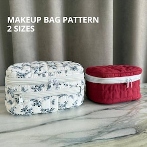 May include: Two quilted makeup bags. One is white with a blue floral pattern, the other is solid red. Both have white zippers. The text "MAKEUP BAG PATTERN 2 SIZES" is at the top of the image.