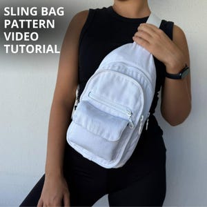 Può includere: Una borsa a tracolla in tela bianca con una tasca frontale con cerniera e uno scomparto con patta. Il testo SLING BAG PATTERN VIDEO TUTORIAL è visibile nell'angolo in alto a sinistra. La borsa presenta una tracolla singola e cerniere argentate.
