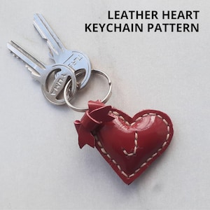 May include: Red leather heart keychain with white stitching. The heart has a bow on the side and is attached to a silver key ring.