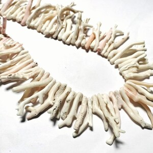 May include: A necklace composed of natural coral pieces. The coral is mainly off-white with some pale pink sections. The coral pieces are arranged in a strand, creating a unique and organic jewellery item.