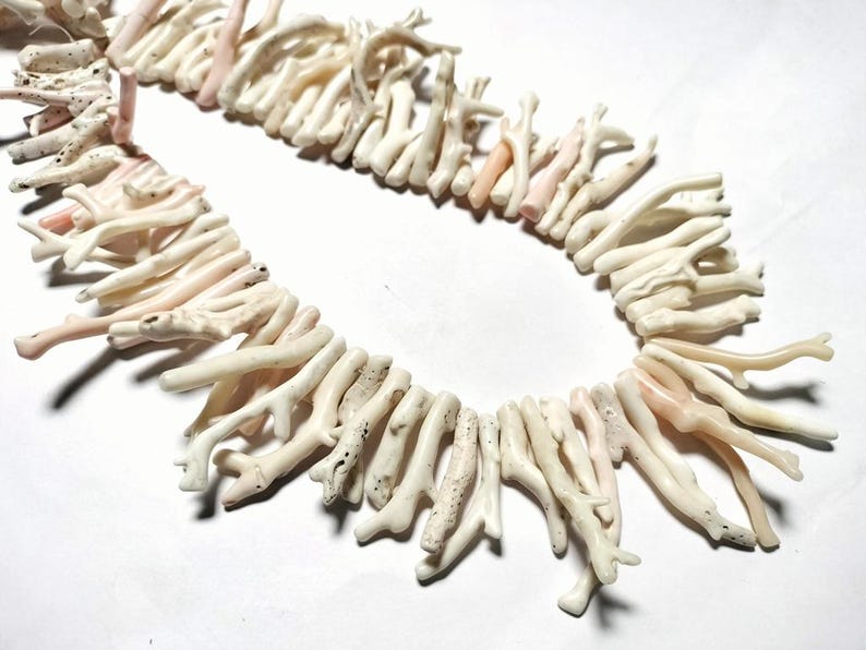 May include: A necklace composed of natural coral pieces. The coral is mainly off-white with some pale pink sections. The coral pieces are arranged in a strand, creating a unique and organic jewellery item.