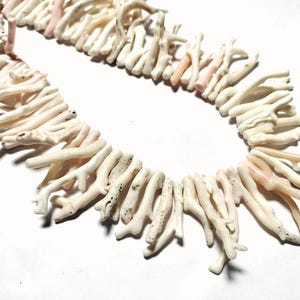 May include: A necklace composed of natural coral branches. The coral is mainly off-white with delicate pink tones. The branches are arranged in a circular design, creating a unique and organic jewellery piece.