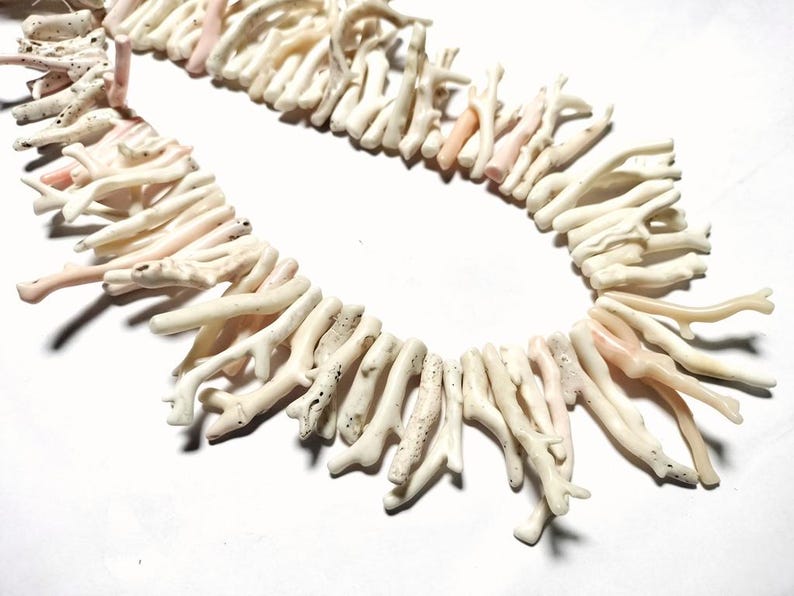May include: A necklace composed of natural coral branches. The coral is mainly off-white with delicate pink tones. The branches are arranged in a circular design, creating a unique and organic jewellery piece.