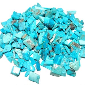 May include: A large collection of small, irregular turquoise stone chips. The pieces are vibrant cyan and light blue in colour, featuring natural dark grey and black matrix inclusions throughout the pile of tumbled, polished gemstone fragments.