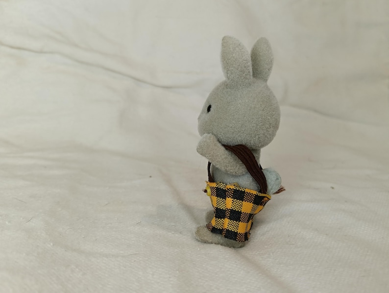 Puede incluir: Figura de conejo gris con una bolsa de correa marr&oacute;n con un patr&oacute;n de cuadros amarillos y negros. El conejo est&aacute; de pie sobre sus patas traseras, con las orejas levantadas. La bolsa cuelga de sus hombros.