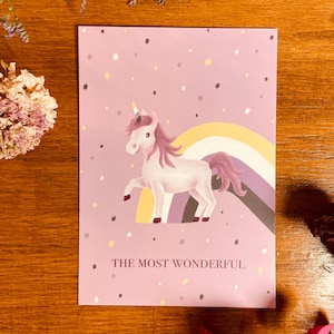 Könnte beinhalten: Ein lila-weißes Einhorn mit einem Regenbogen dahinter. Das Einhorn hat ein gelbes Horn und eine rosafarbene Mähne. Der Hintergrund ist helllila mit weißen und schwarzen Punkten. Der Text "THE MOST WONDERFUL" ist unterhalb des Einhorns gedruckt.
