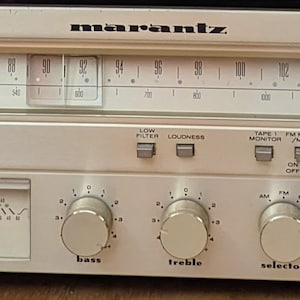 Puede incluir: Un receptor estéreo vintage Marantz SR 1010 plateado con una grabadora de casetes negra y plateada. El receptor tiene una placa frontal plateada con letras y botones negros. El receptor tiene un sintonizador, una grabadora de casetes y un preamplificador.
